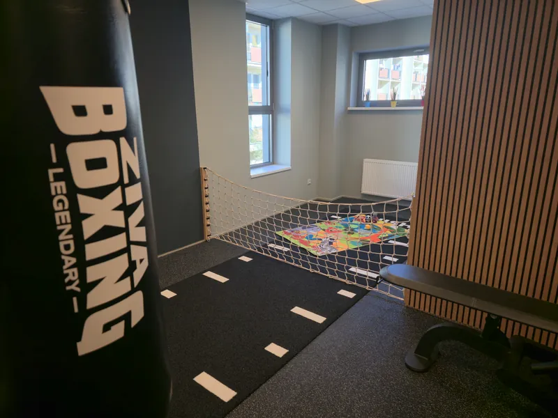 Posilovna 01.fitness s boxovacím pytlem a dětským koutkem za sítí v pozadí